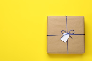 Photo of Parcel wrapped in kraft paper with tag on yellow background, top view. Space for text