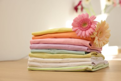 Photo of Stack of clean clothes and flowers on wooden table