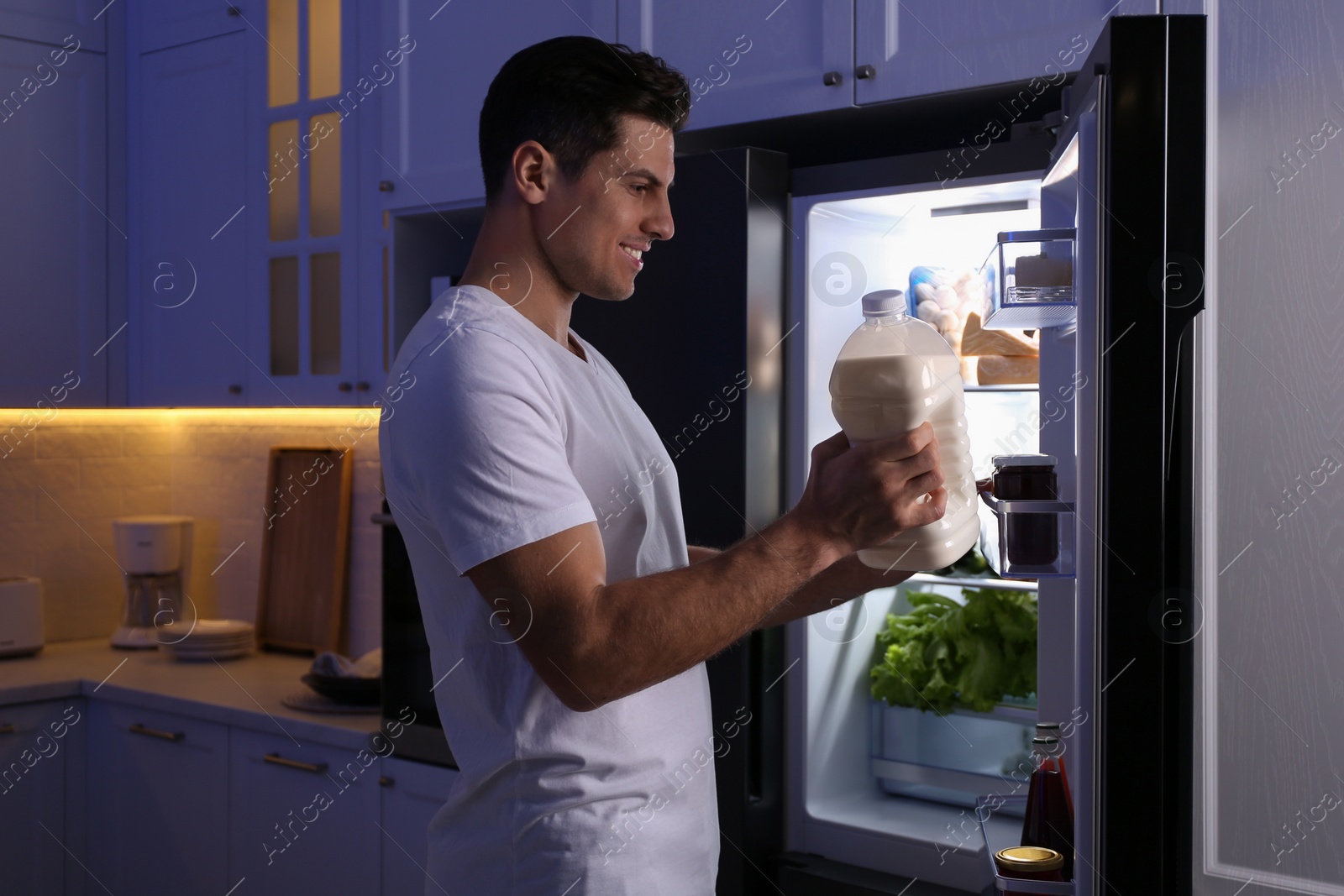 Photo of Man holding gallon bottle of milk near refrigerator in kitchen at night