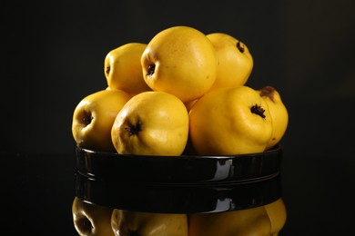 Photo of Tasty ripe quinces in bowl on black mirror surface