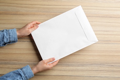 Woman holding paper envelope on wooden background, closeup
