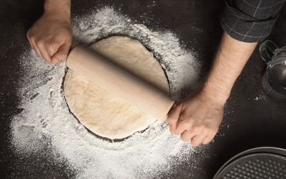 Photo of Man rolling dough for pizza on table