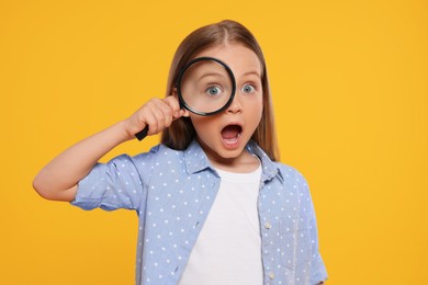 Photo of Cute little girl looking through magnifier on yellow background