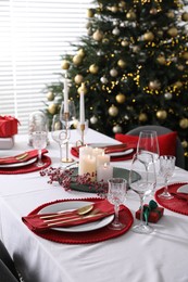 Christmas table setting with burning candles, gift box and dishware indoors