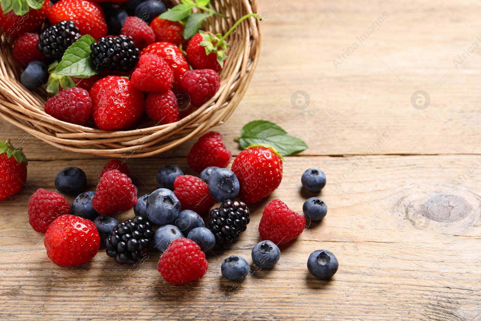 Photo of Wicker basket with many different fresh ripe berries on wooden table, space for text