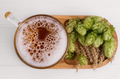 Photo of Mug with beer, fresh hops and ears of wheat on white wooden table, top view