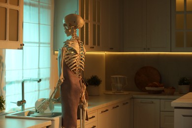 Photo of Human skeleton washing dishes in kitchen sink at night