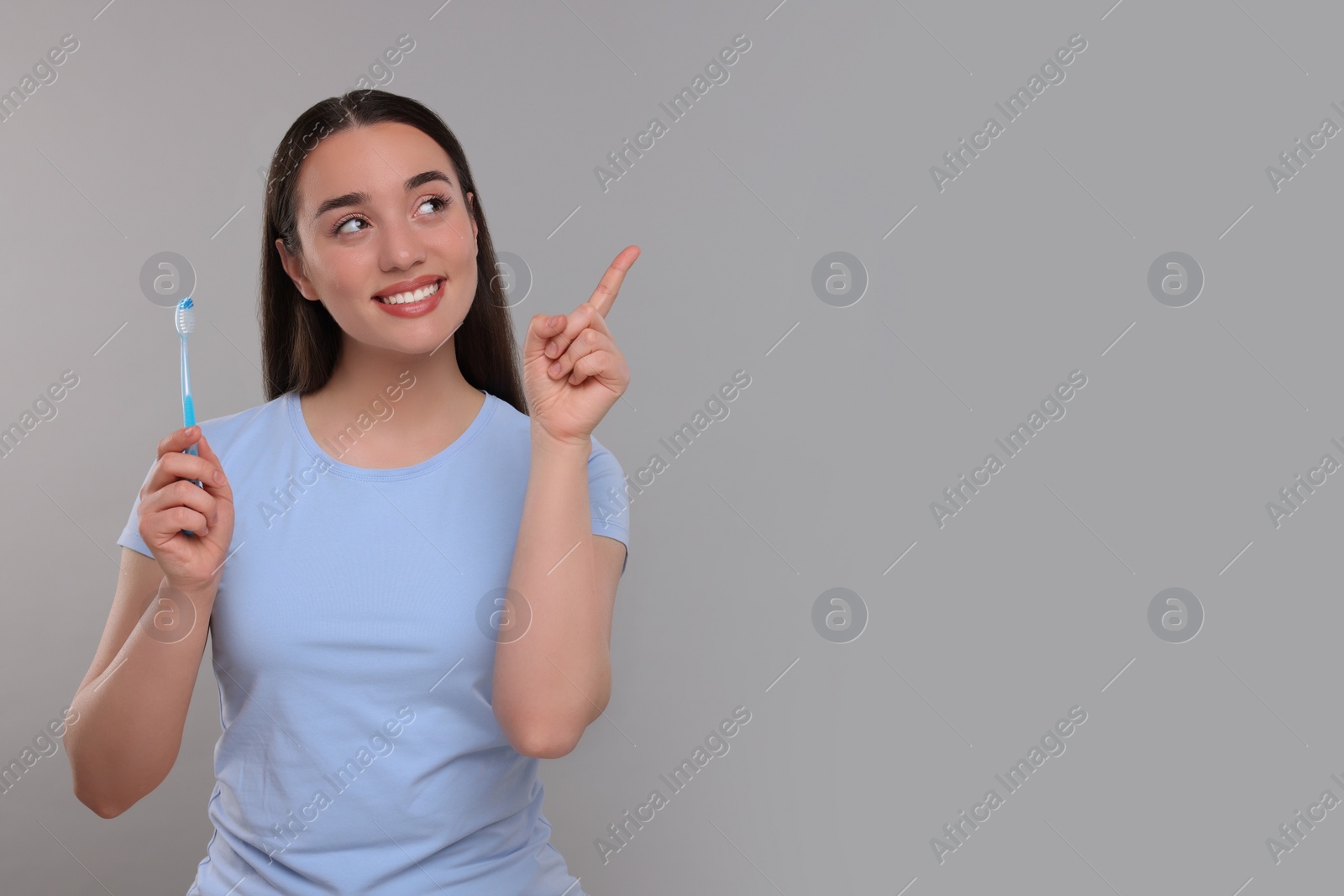 Photo of Happy young woman holding plastic toothbrush and pointing on light grey background, space for text