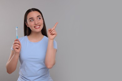 Happy young woman holding plastic toothbrush and pointing on light grey background, space for text