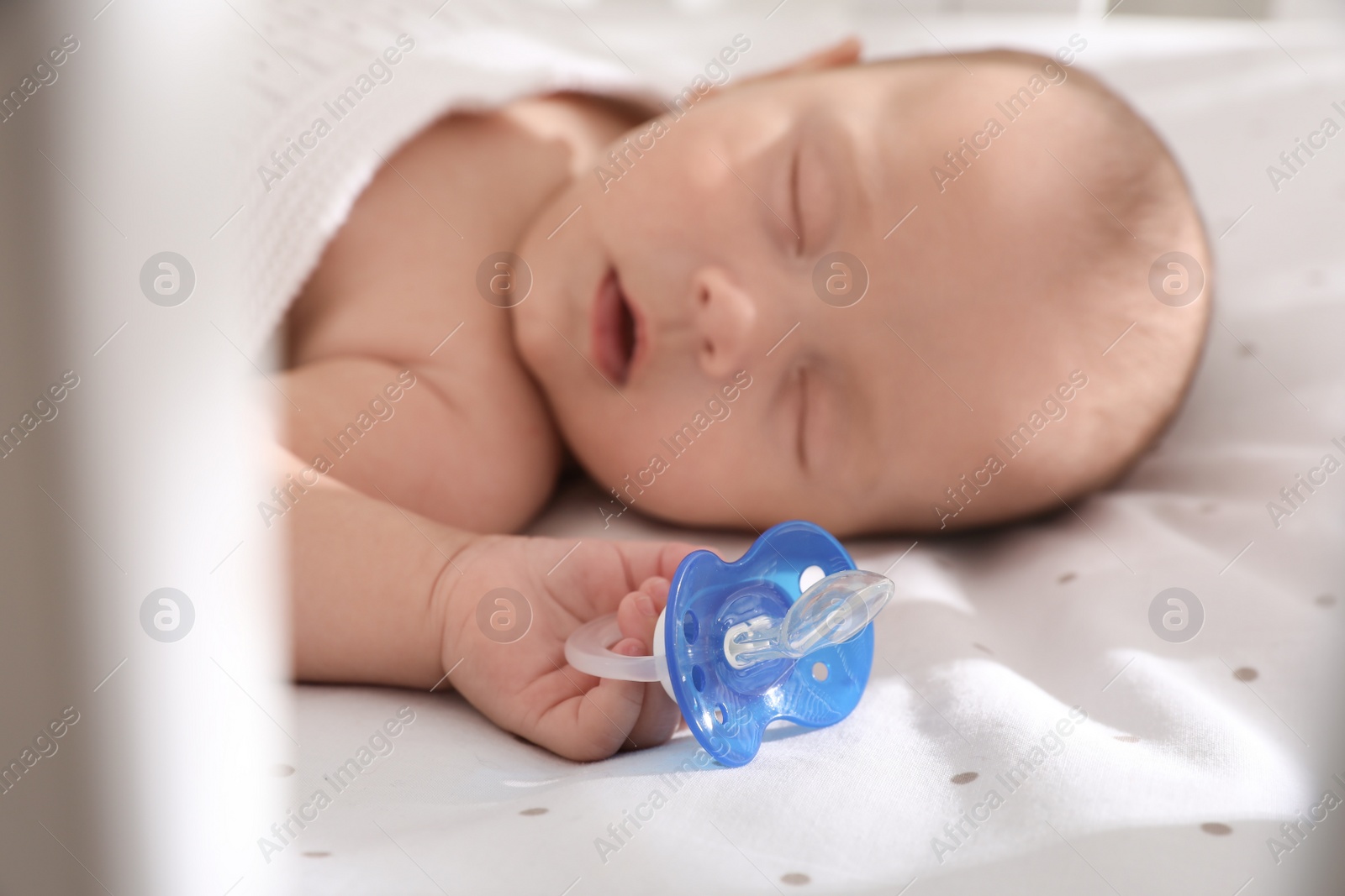 Photo of Cute little baby sleeping in bed, focus on hand with pacifier