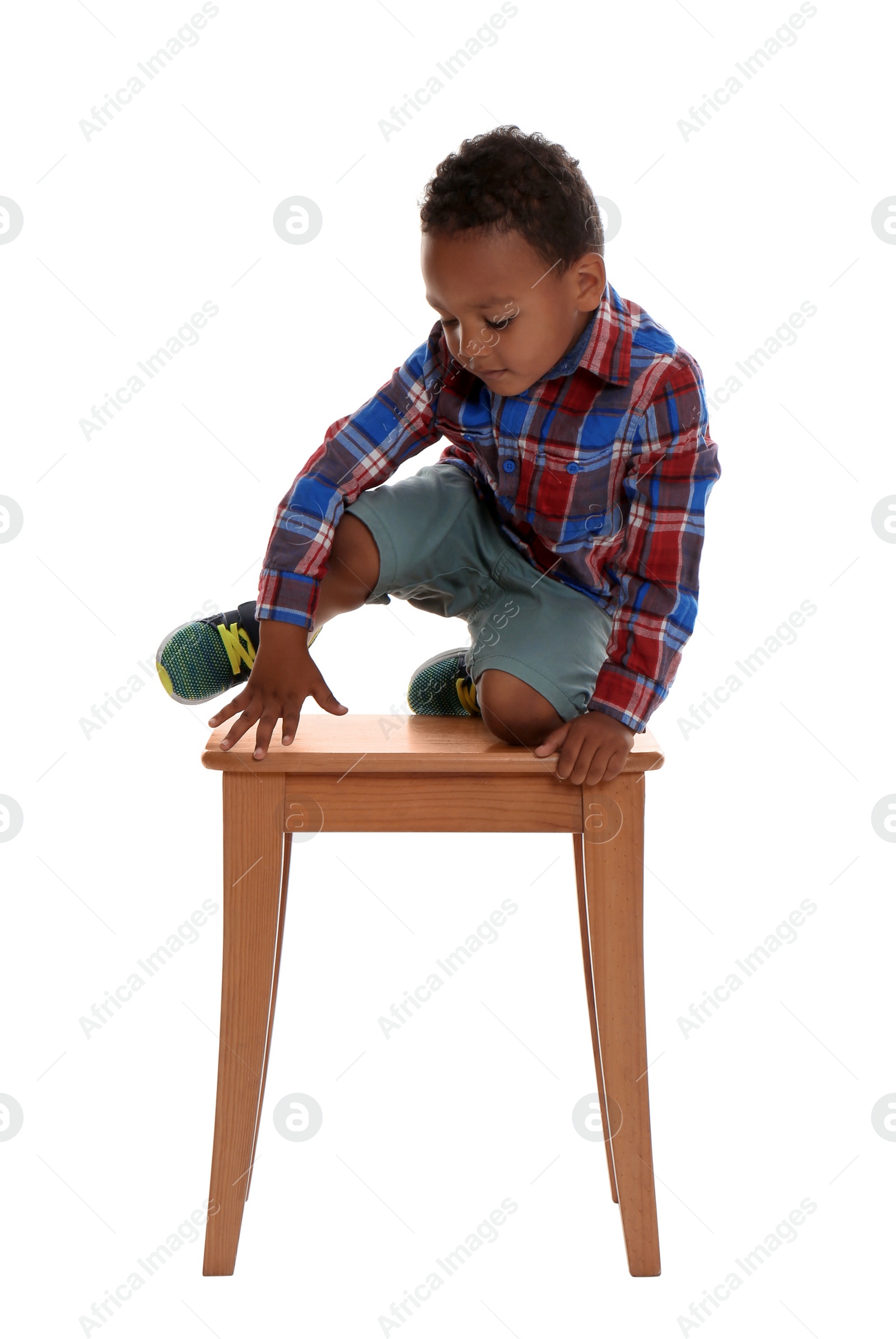 Photo of Little African-American boy climbing up stool on white background. Danger at home