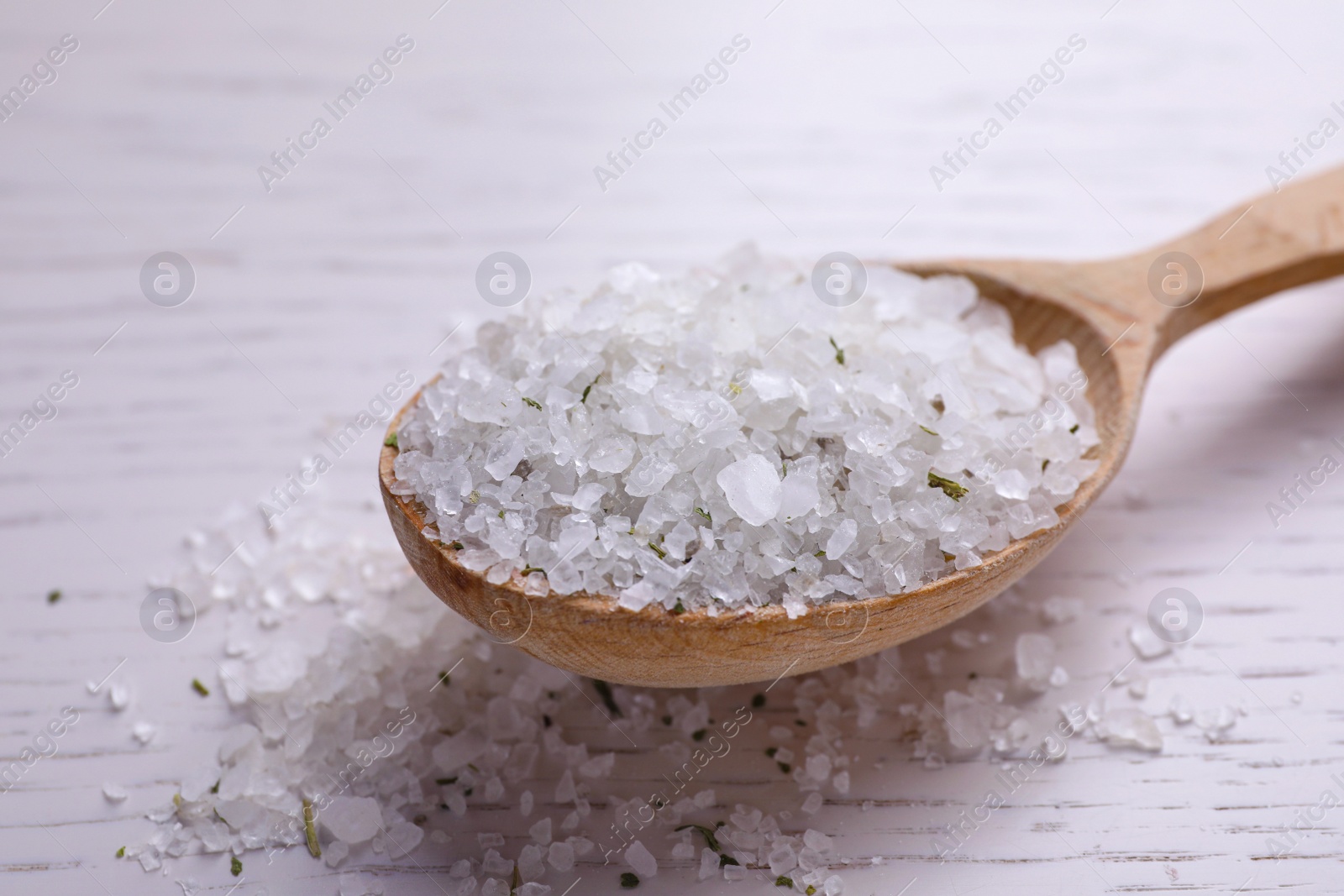 Photo of Spoon with sea salt on white wooden table, closeup. Spa treatment