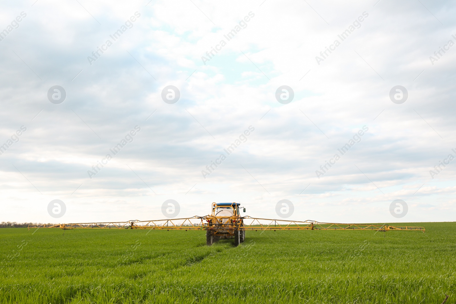 Photo of Tractor spraying pesticide in field on spring day. Agricultural industry