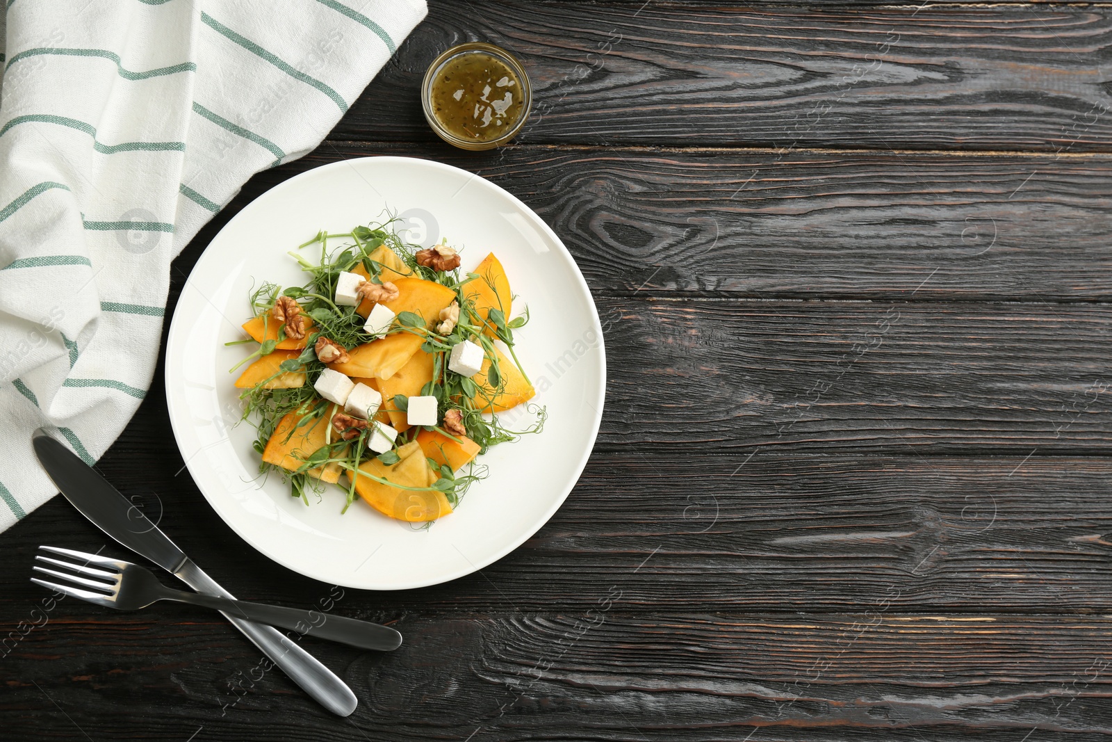 Photo of Delicious persimmon salad with feta cheese and walnuts served on wooden table, flat lay. Space for text