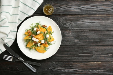 Delicious persimmon salad with feta cheese and walnuts served on wooden table, flat lay. Space for text