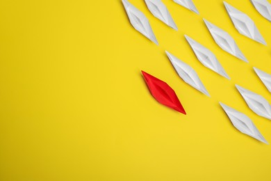 Red paper boat among others on yellow background, flat lay with space for text. Uniqueness concept