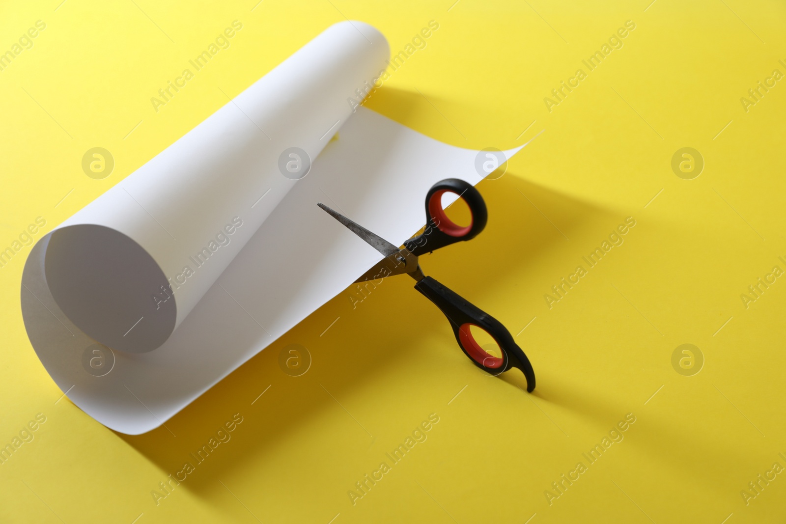 Photo of Scissors cutting white paper on yellow background. Space for text