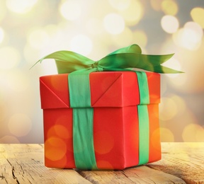 Image of Christmas gift box on wooden table against blurred background, bokeh effect