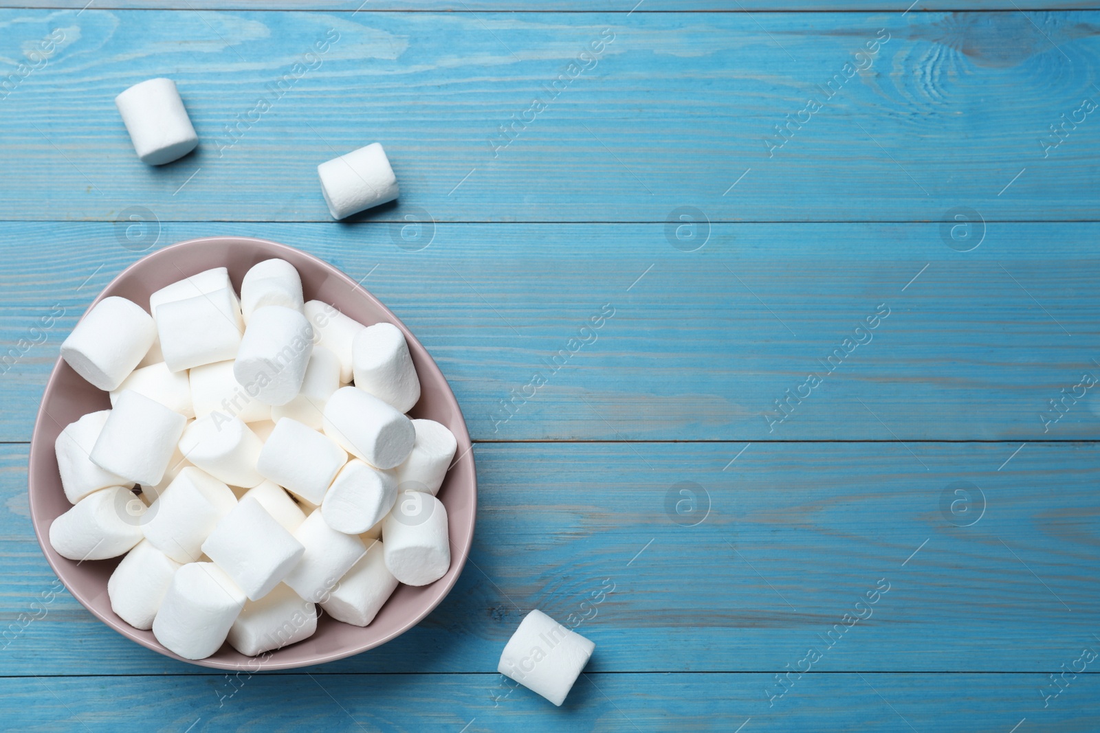 Photo of Delicious puffy marshmallows on light blue wooden table, flat lay. Space for text