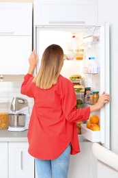 Young woman choosing food from refrigerator in kitchen. Healthy diet