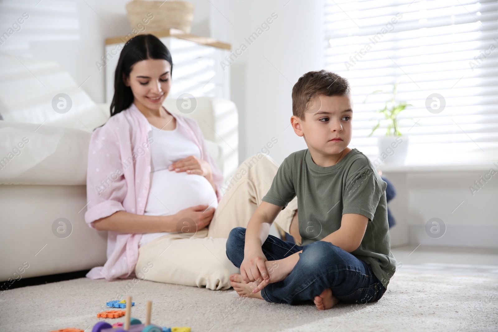 Photo of Unhappy little boy near pregnant mother at home. Feeling jealous towards unborn sibling