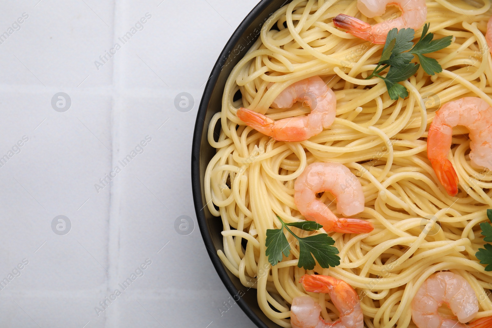 Photo of Tasty spaghetti with shrimps and parsley in bowl on light tiled table, top view. Space for text