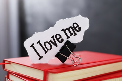 Photo of Piece of paper with handwritten phrase I Love Me and clip on notebook stack, closeup