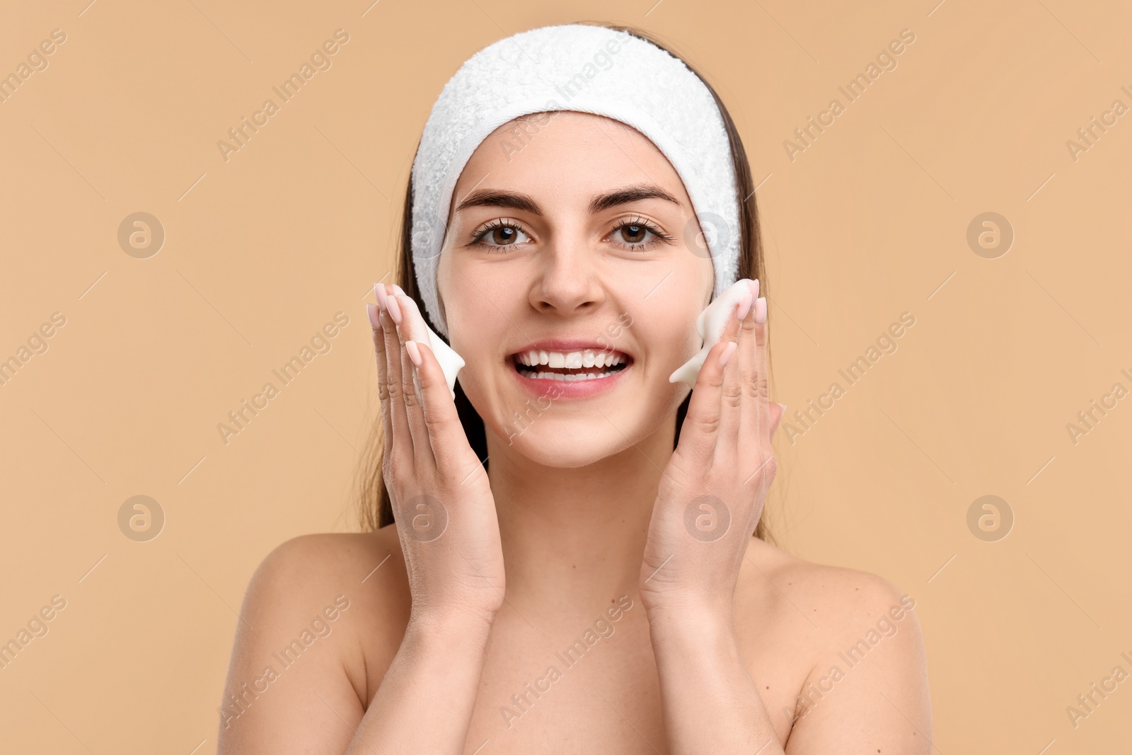 Photo of Young woman with headband washing her face on beige background