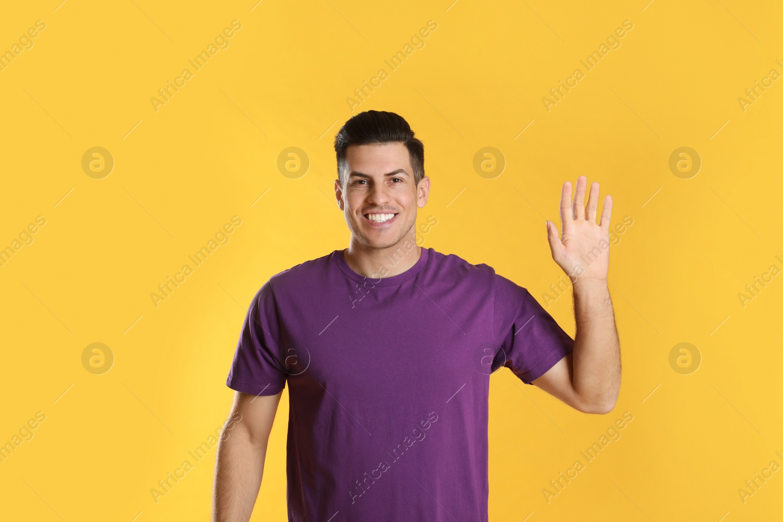 Photo of Cheerful man waving to say hello on yellow  background