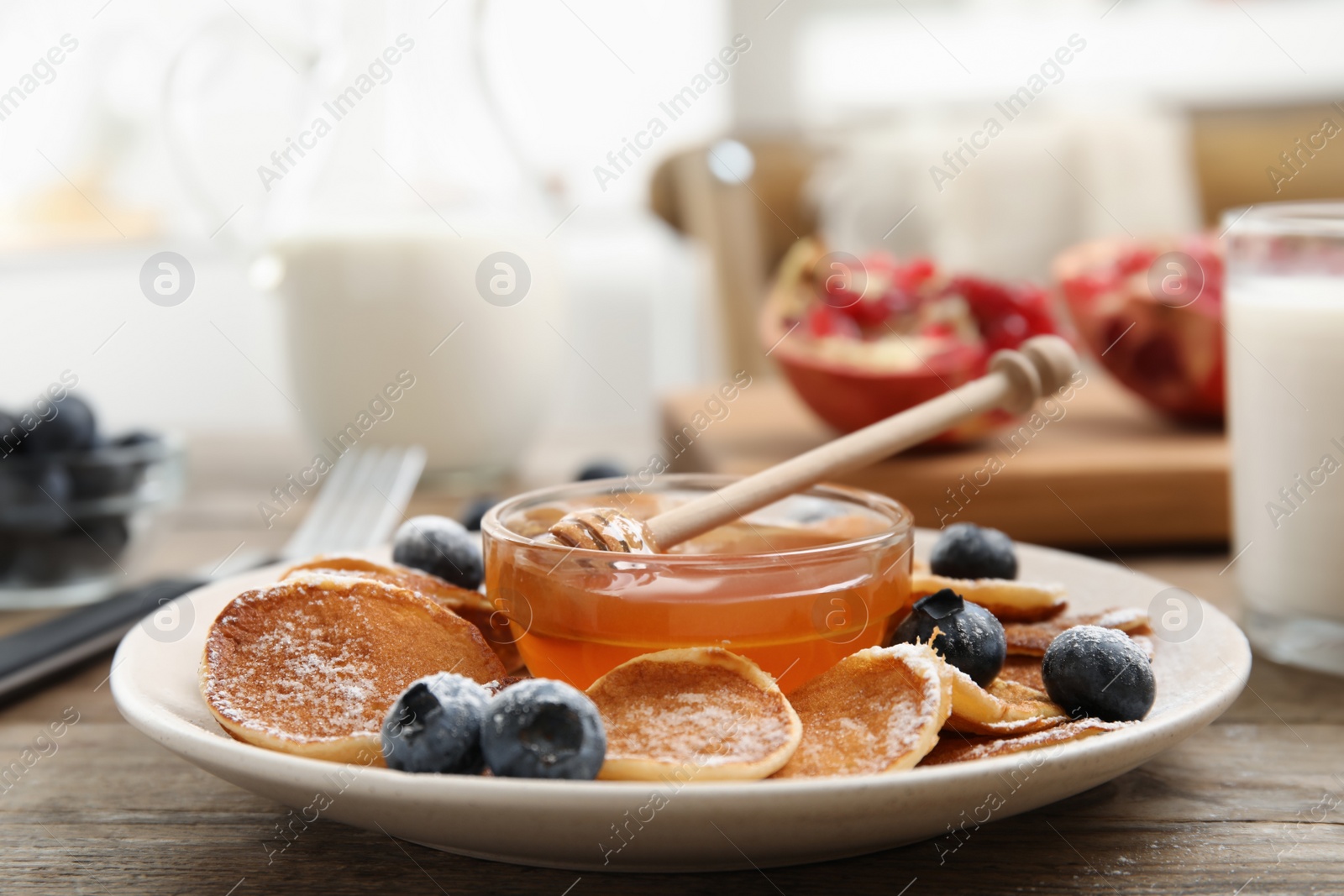 Photo of Delicious mini pancakes cereal with blueberries and honey served on wooden table