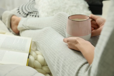 Photo of Woman with cup of coffee and book sitting on soft plaid, closeup