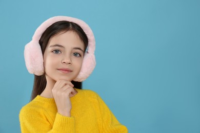 Photo of Cute little girl wearing stylish earmuffs on light blue background. Space for text