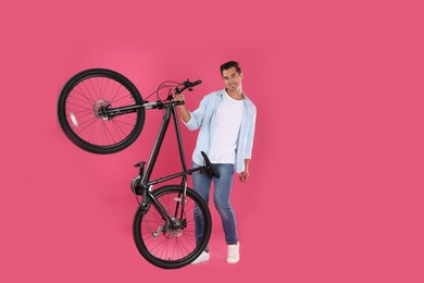 Handsome young man with modern bicycle on pink background