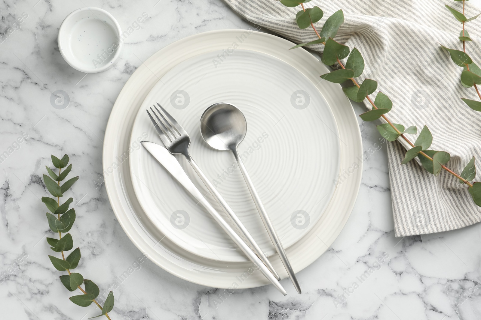 Photo of Stylish setting with cutlery, napkin, eucalyptus branches and plates on white marble table, flat lay