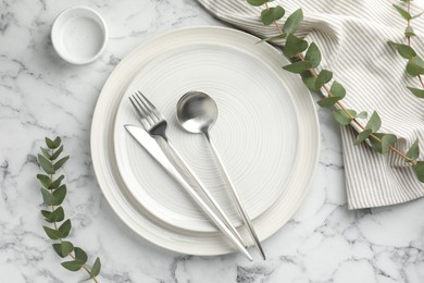 Photo of Stylish setting with cutlery, napkin, eucalyptus branches and plates on white marble table, flat lay