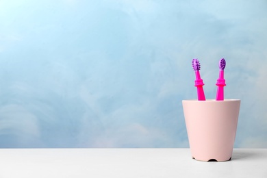 Baby toothbrushes in holder on table against color background with space for text