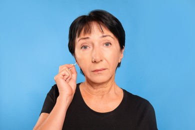 Photo of Senior woman cleaning ear with cotton swab on light blue background