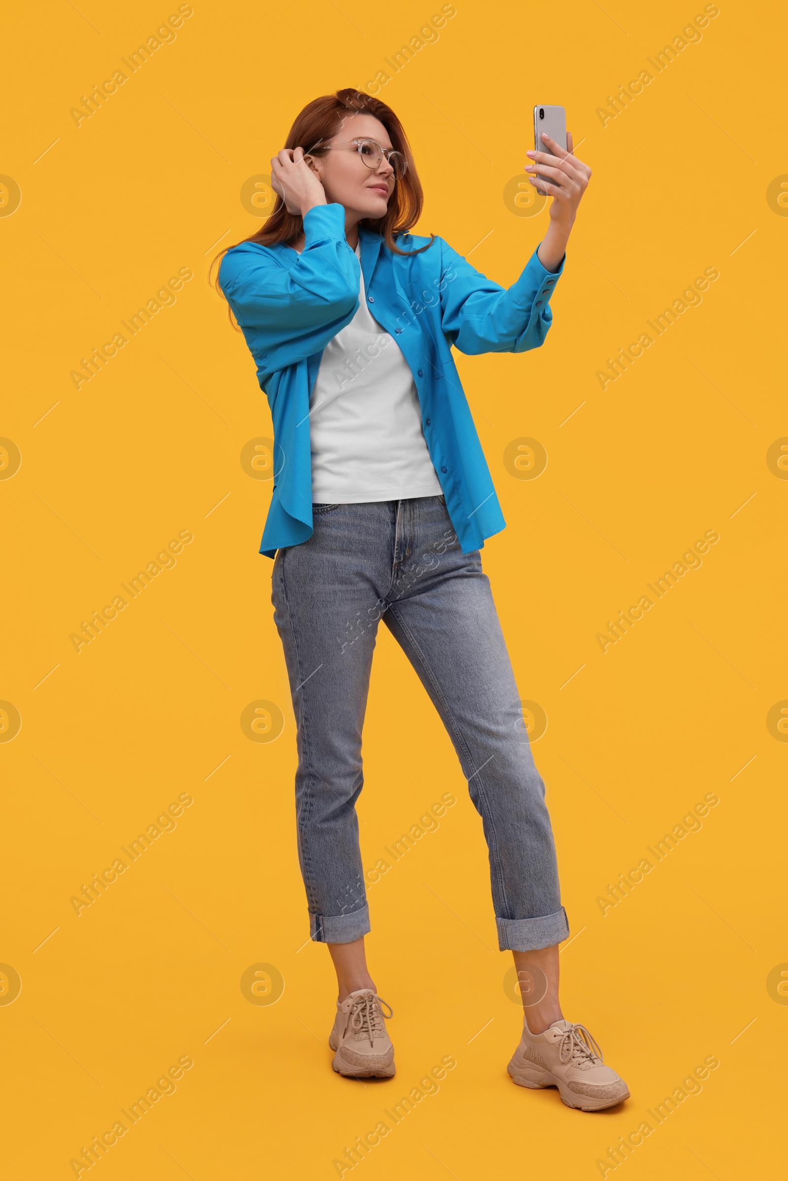 Photo of Beautiful woman in eyeglasses taking selfie on orange background