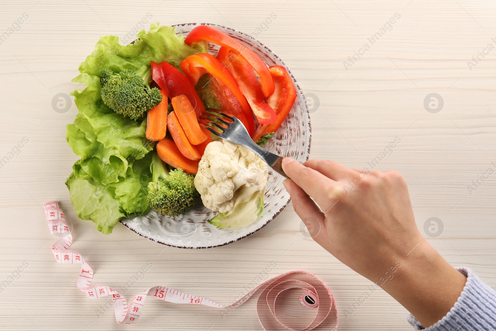 Photo of Healthy diet. Woman eating fresh vegetables at light wooden table, top view