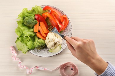 Photo of Healthy diet. Woman eating fresh vegetables at light wooden table, top view