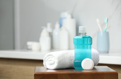 Photo of Bottle of mouthwash, towel and dental floss on wooden table in bathroom, space for text