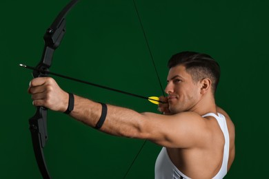 Man with bow and arrow practicing archery on green background