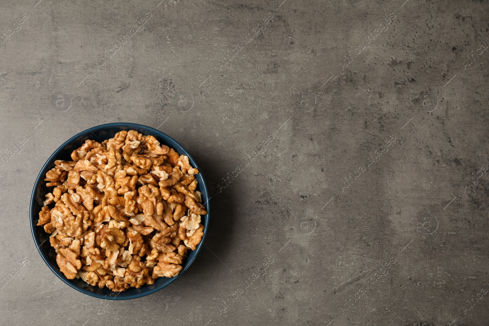 Photo of Dish with walnuts on grey background, top view. Space for text