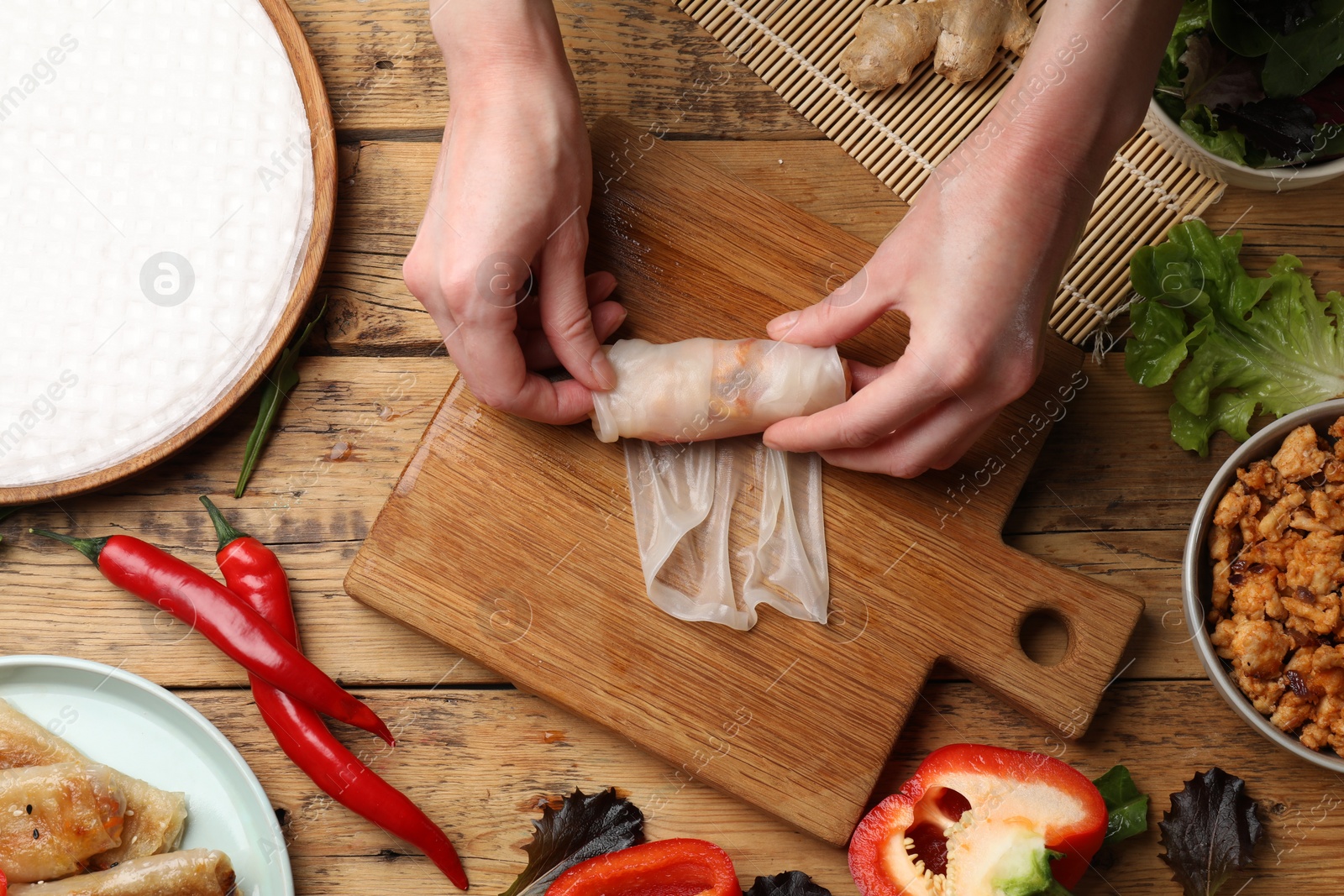 Photo of Woman making tasty spring roll at wooden table, top view