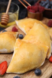 Delicious samosas and berries on wooden board, closeup