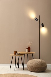 Knitted pouf, lamp and decor elements near beige wall indoors. Space for text