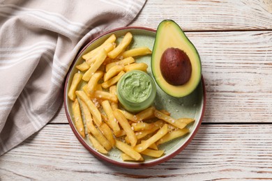 Photo of Plate with french fries, guacamole dip and avocado served on white wooden table, top view