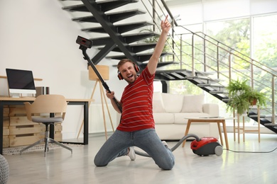 Young man having fun while vacuuming in living room