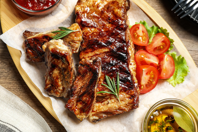 Photo of Delicious grilled ribs served on wooden table, flat lay