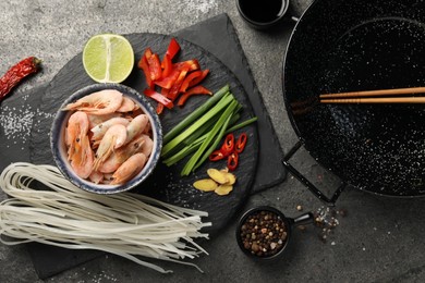 Flat lay composition with black wok, spices and products on dark textured table